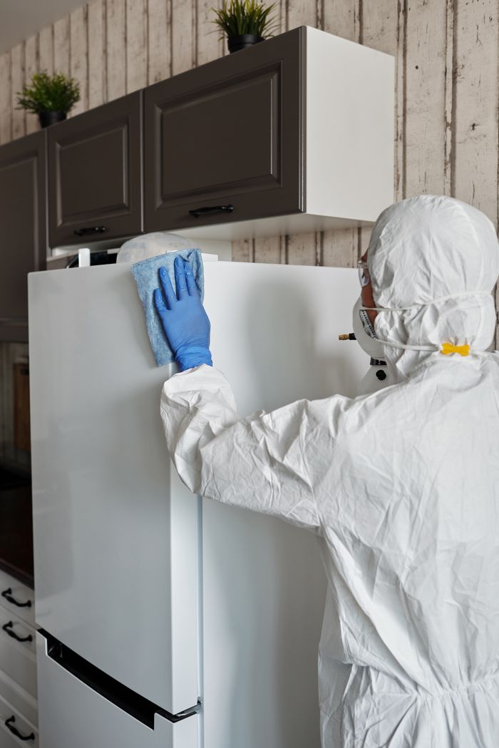 about-us-01 Healthcare worker in protective gear disinfects a refrigerator to ensure safety and cleanliness.